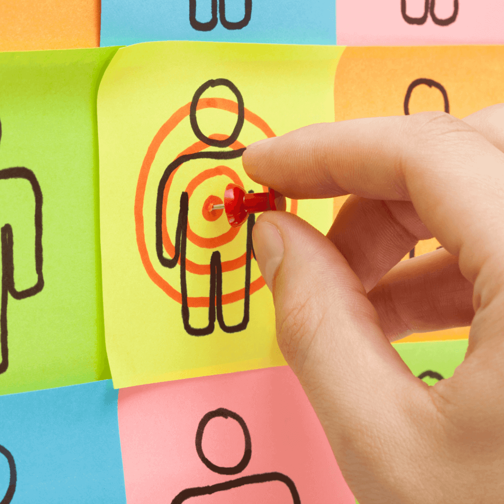 A picture of someone putting a tack into a sticky note that has a drawing of a person, indicating a bullseye.