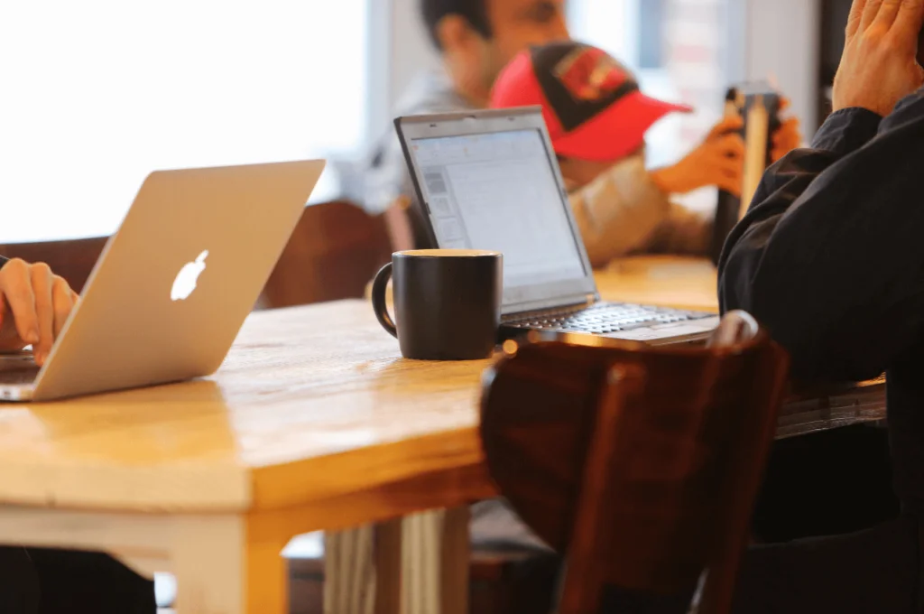 A group of people sitting at a coffee shop table, working on their computers.