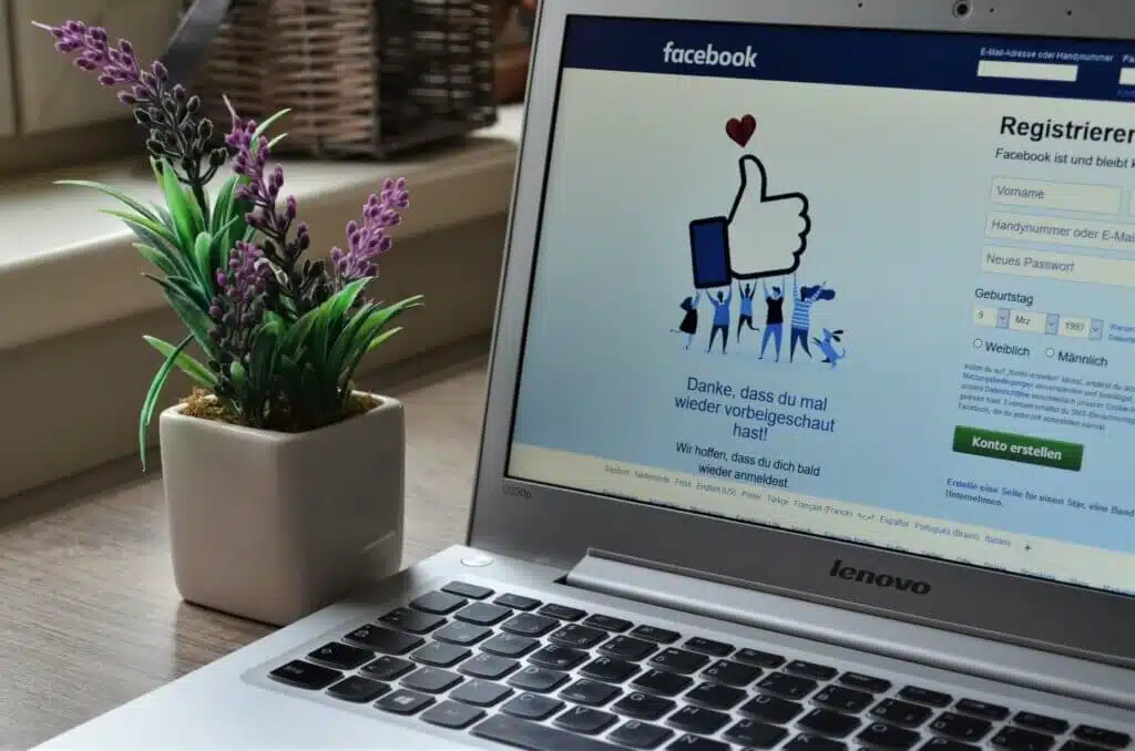 Closeup of a laptop with Facebook pulled up. There's a purple flower in the background.
