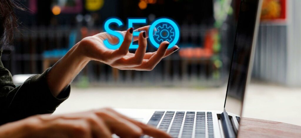 A zoomed in shot of a woman's hands next to a computer. Her left hand is holding the word "SEO"