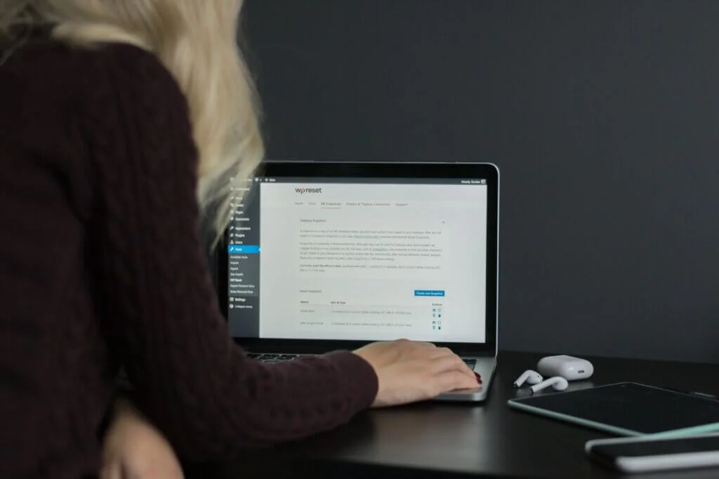 A picture of a girl using Macbook Pro to reset her WordPress site with a free plugin.

