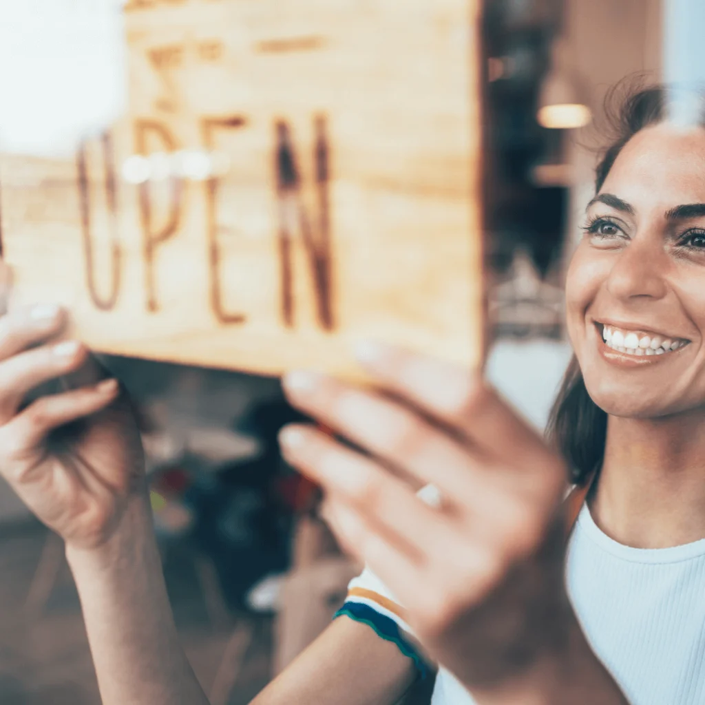 A female small business owner putting an "open" sign on her business's door