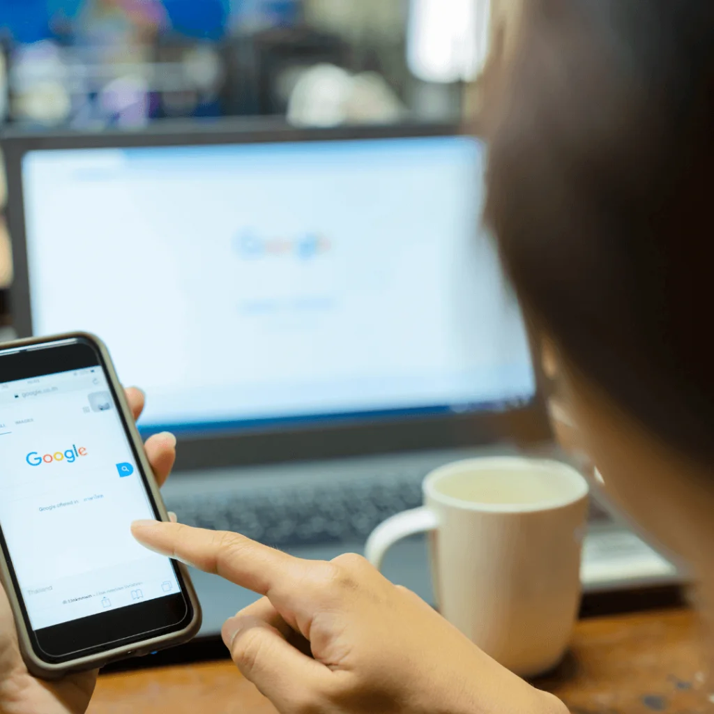 A person holding a phone with the Google website displayed on the screen