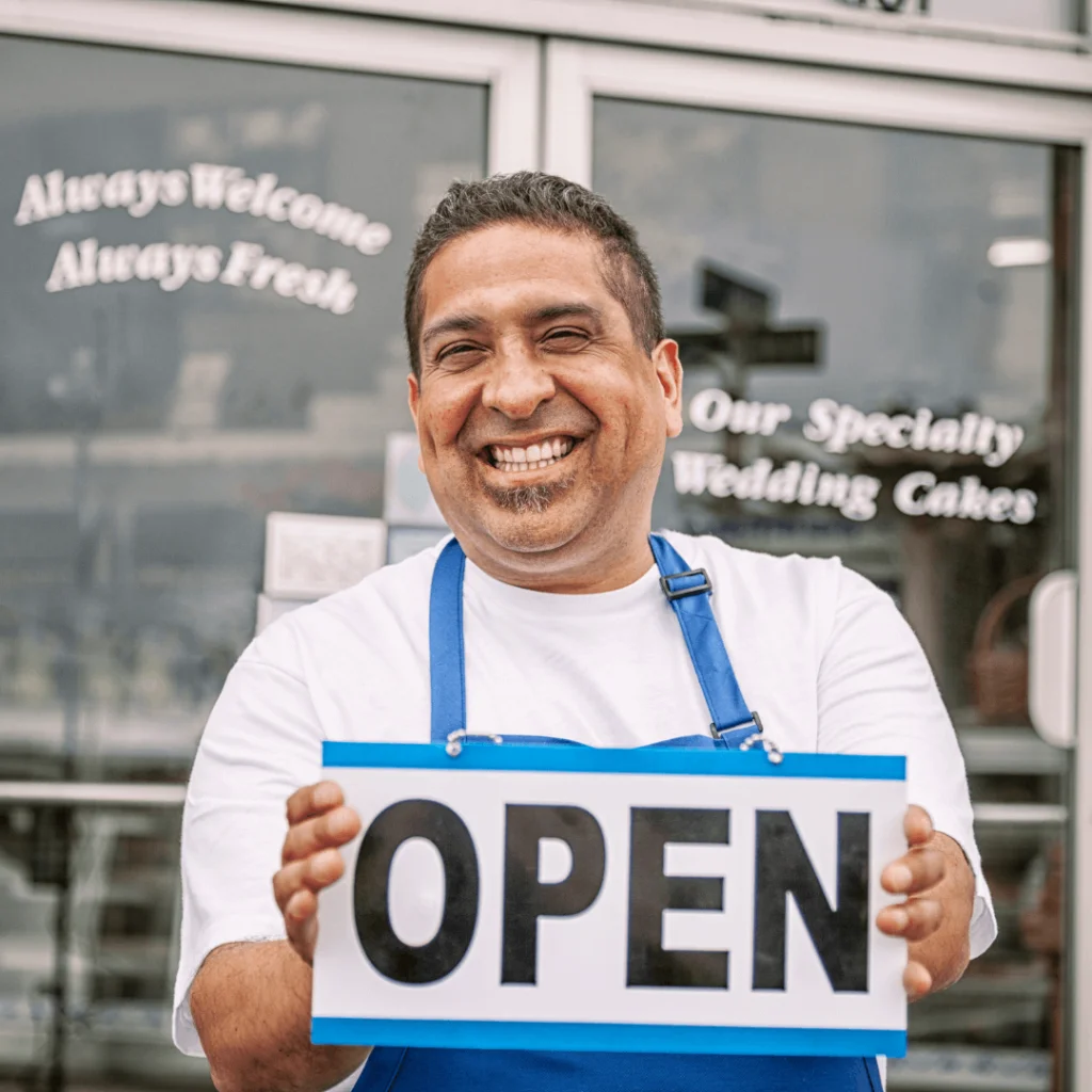 A man holding an "Open" sign standing in front of a storefront