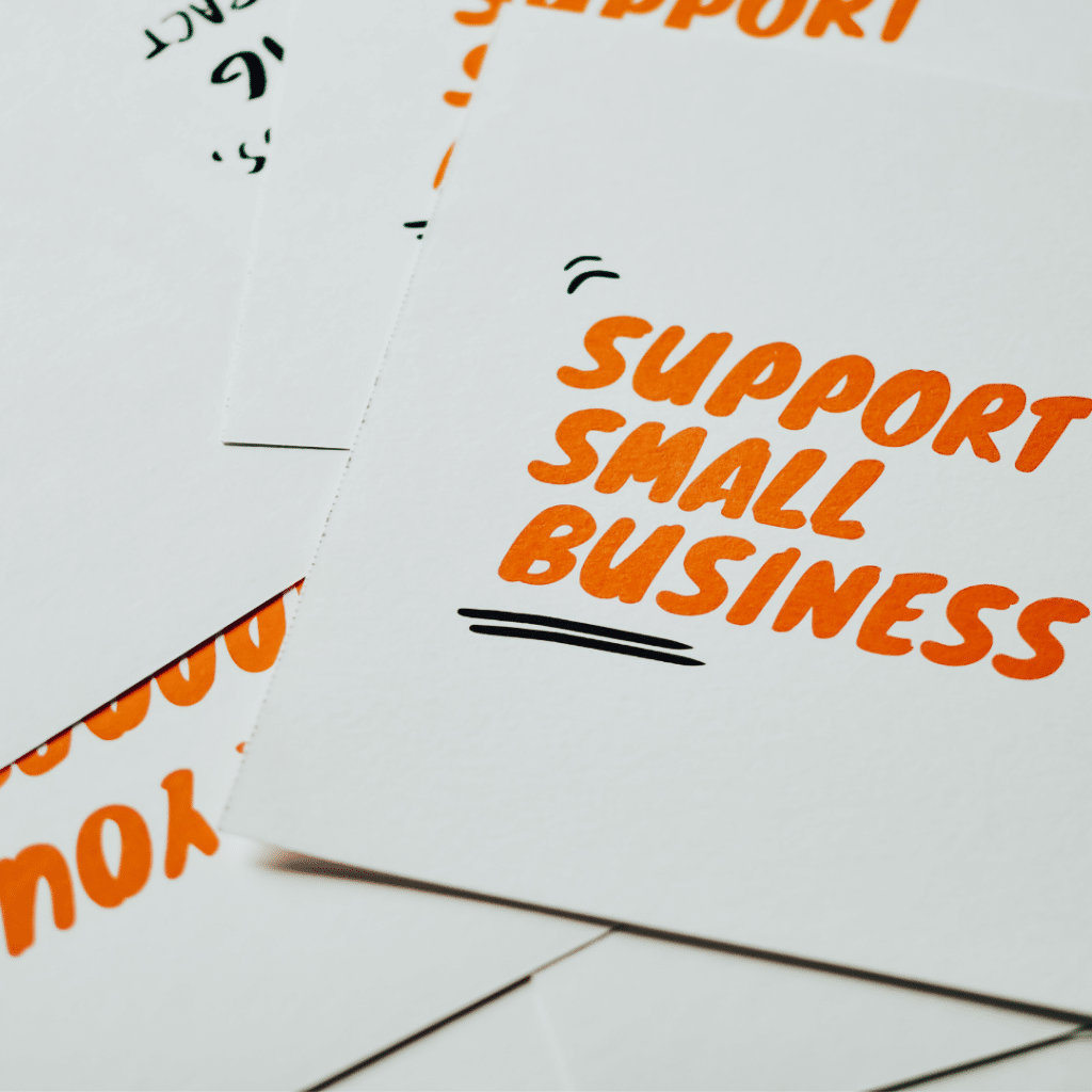 Cards are piled on a table with "Support Small Business" written on them in orange text.