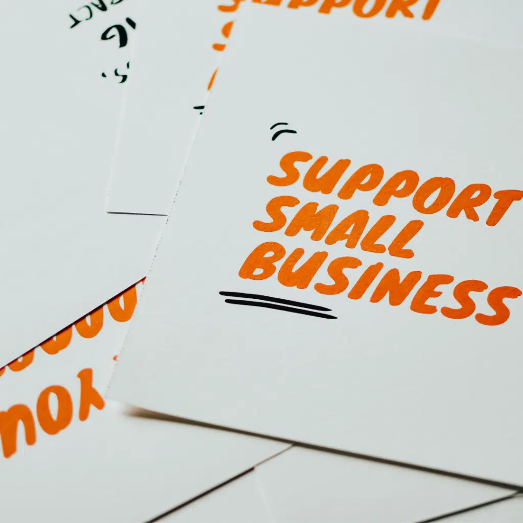 Cards are piled on a table with "Support Small Business" written on them in orange text.